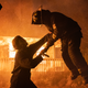 Michael Myers lifts a firefighter up in front of a burning house in a scene from Halloween Kills.